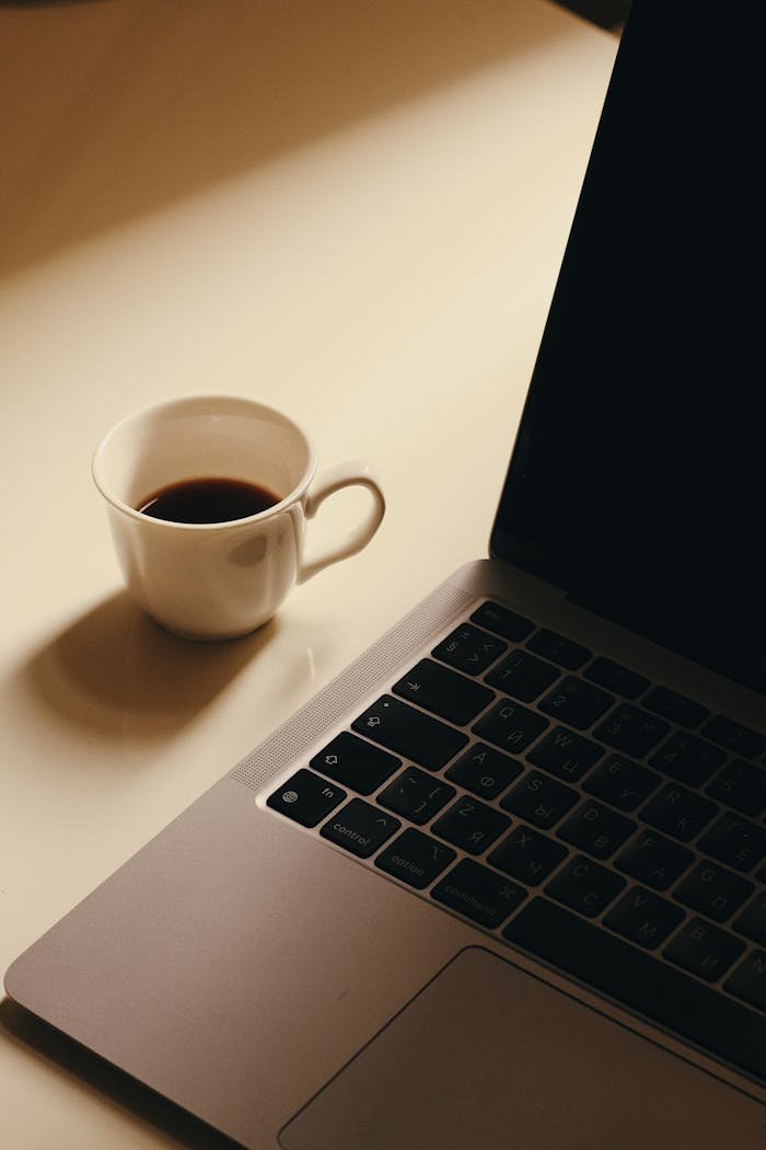 A minimalist workspace featuring a cup of coffee next to a laptop on a light-colored desk.