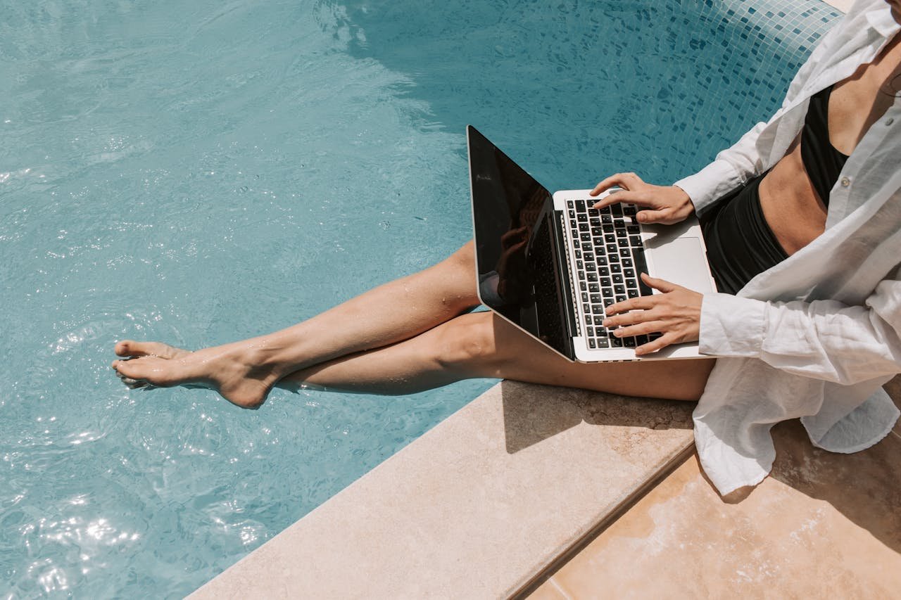 A woman in swimwear working on a laptop by the pool, showcasing summer remote work lifestyle.